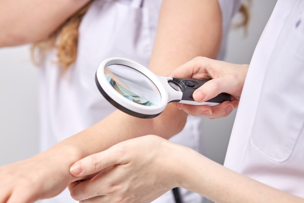 Dermatologist using a professional magnifying glass while doing skin examination to female patient